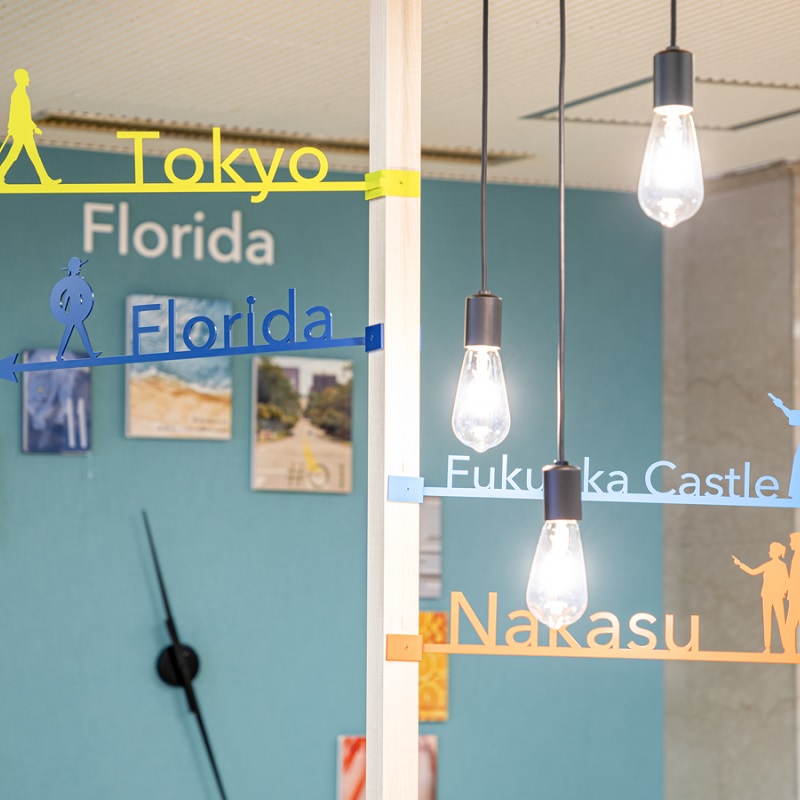 Comfort Library Cafe interior showing travel-themed wall directional signs for Tokyo, Florida, Nakasu, and Fukuoka Castle